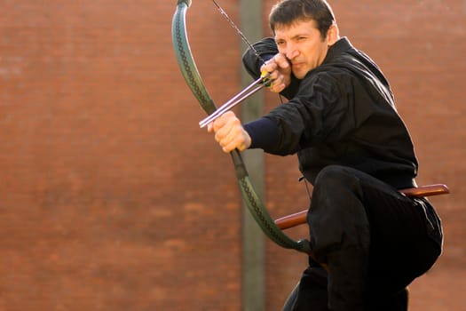 Man in black kimono is practicing archery with traditional Hungarian bow and two arrows.