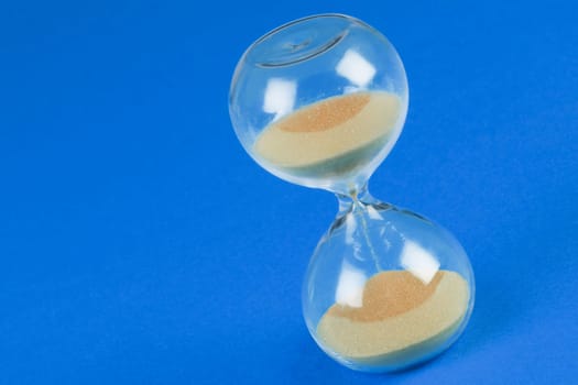 Sand clock hourglass on blue background, out of time concept.