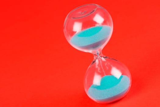 Blue sand clock hourglass on orange background, out of time concept.