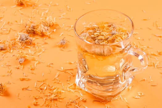 Herbal tea of dried marigold petals on orange background.