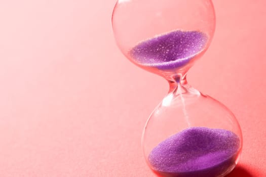 Purple sand clock hourglass on pink background, out of time concept.