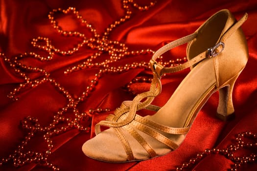 Golden latin dance shoe is on red satin background with red pearls.
