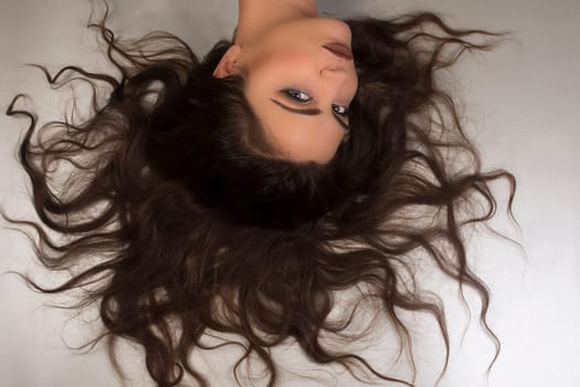 Beautiful woman is lying down with her long brown hair on gray background.