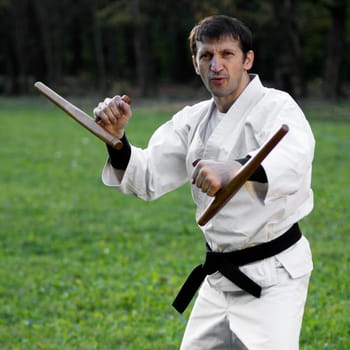 Master of martial arts in white kimono is practicing with tonfa.