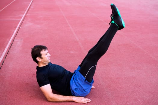 The athlete is exercising abdominal or stomach outdoors in stadium.