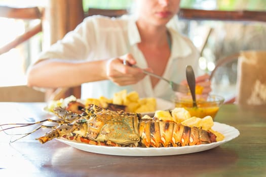 Lady on tropical vacations eating grilled lobster served with potatoes and coconut sauce.