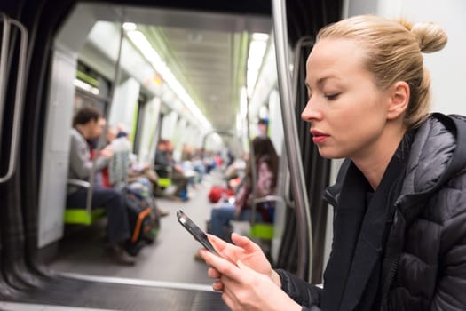 Young girl reading from mobile phone screen while traveling on metro. Wireless internet on public transport concept.