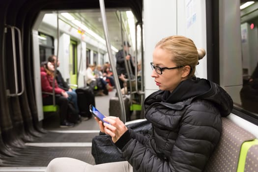 Cheerful young girl texting on mobile phone social network applications while traveling on metro. Wireless internet on public transport concept.