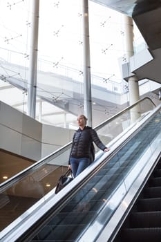 Young businesswoman with large black bag and mobile phone getting down on the escalator during business trip in modern city.