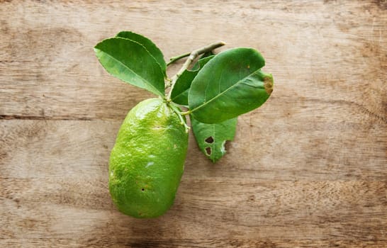 Top view fresh organic lemon with leaves on wooden table background, imperfect insect bites, pesticide free.
