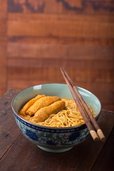 Hot and spicy Curry Noodle Soup with chopsticks on wooden table, Malaysian cuisine.
