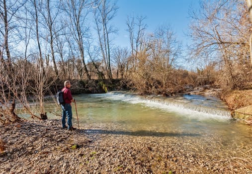 Hiker of about 60 years, on the bank of the stream overlooking a small waterfall.