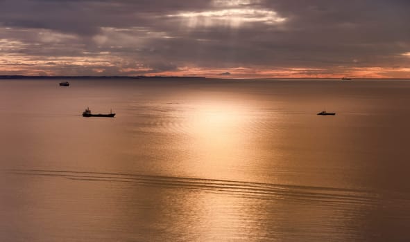 Seascape with ships at sunset with cloudy sky.