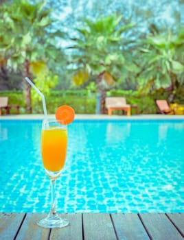 Orange juice with carrot slice in cocktail glass at outdoor swimming pool, summer tropical holiday concept. Vintage filtered image.