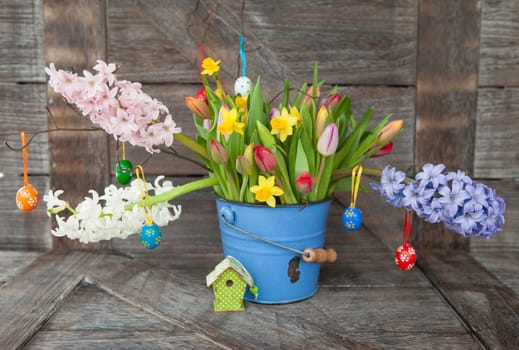 Colorful spring flowers in blue bucket on background of rustic wood