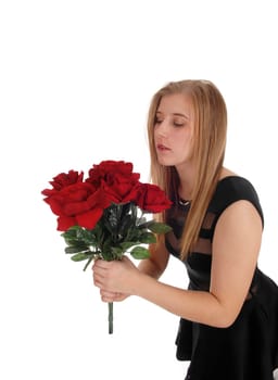 A gorgeous woman in a black dress standing in profile with a big.bunch of red roses with her eyes closed, isolated for white background.