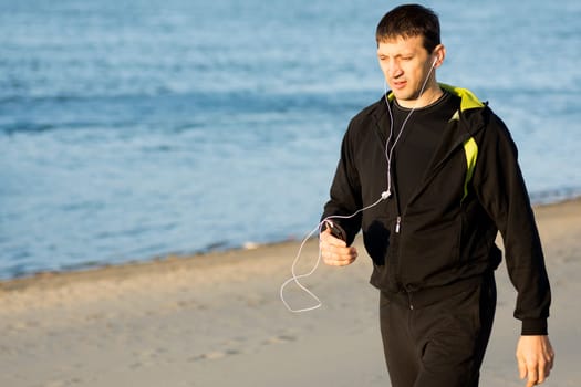 The man in sportswear with earphones is jogging outdoors on the beach.