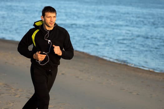 The man in sportswear with earphones is jogging outdoors on the beach.