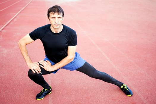 The athlete is exercising and stretching legs in the stadium.