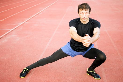 The athlete is exercising and stretching legs in the stadium.
