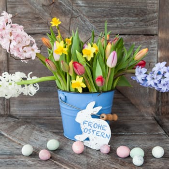 Colorful spring flowers in blue bucket on background of rustic wood