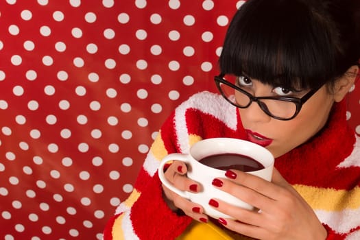 Young woman in vintage style is drinking hot drink from cup on red dotted background with white circles.