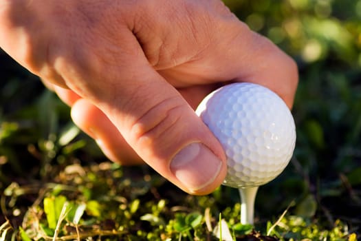 Macro photo of male hand with golf ball in the grass.