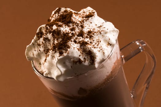 Hot chocolate drink or milkshake with whipped cream on brown background.