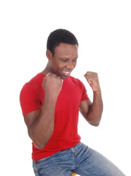 A young handsome African American man sitting in a red shirt with.his fists and smiling of victory and success, isolated over white.