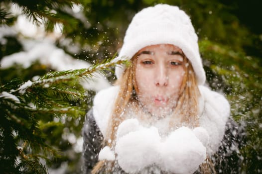 Blowing Snow. Beautiful Joyful Female Model on background of fir trees. Young woman enjoying magical snowfall. Winter wonderland.