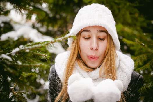 Blowing Snow. Beautiful Joyful Female Model on background of fir trees. Young woman enjoying magical snowfall. Winter wonderland.