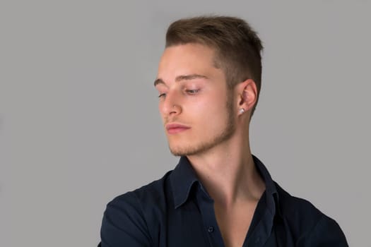 Sad, depressed blond young man looking down. Light grey background