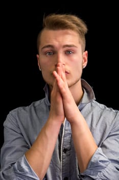 Attractive blond young man, serious expression with hands joined in front of mouth