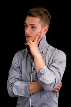 Attractive young man thinking, looking away with hand on his chin, on black background