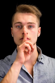 Attractive young man gesturing Hush or Silence with finger on mouth and nose