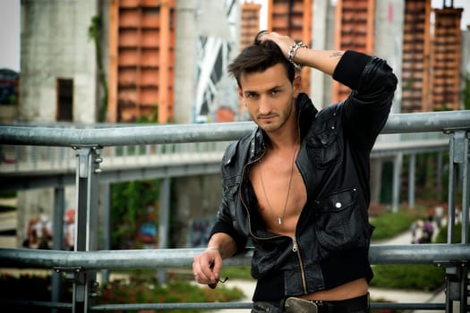 Handsome man outdoor in urban environment wearing leather jacket on naked torso