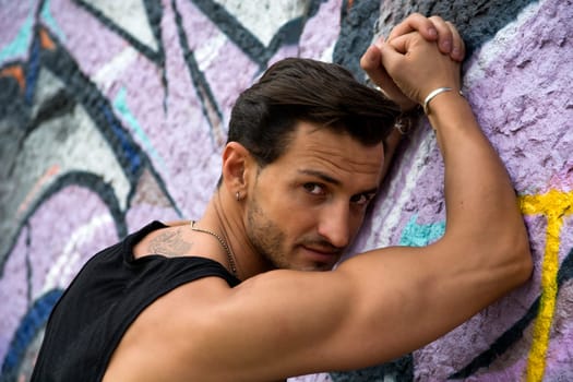 Handsome man leaning against colorful graffiti wall