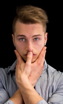 Attractive blond young man, serious expression with hands joined in front of mouth