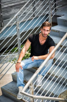 Handsome bearded young man sitting outdoors in urban environment looking at camera