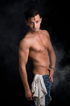 Handsome lean man wearing blue jeans on dark smoky background
