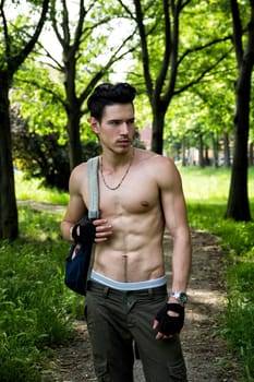 Handsome young man shirtless outdoors hiking on park path with backpack on shoulder
