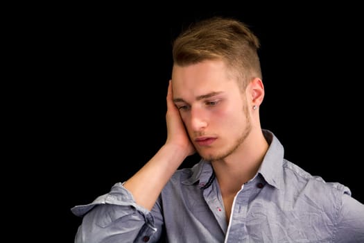 Sad or worried handsome young man looking down, isolated on black