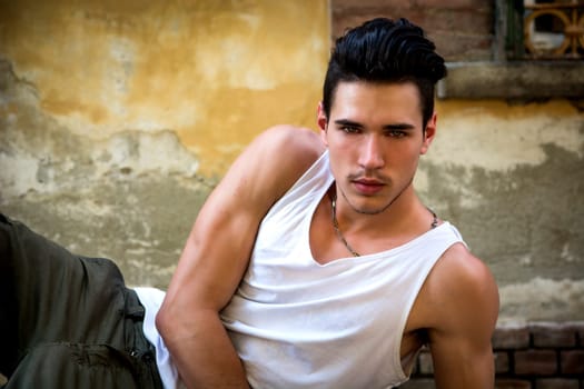 Attractive young man laying down, wearing white tank-top outdoors, looking at camera