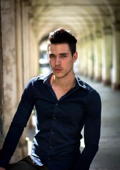 Handsome young man standing outdoors under old colonnade in european town