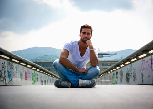 Handsome bearded young man sitting outdoors in urban environment looking at camera