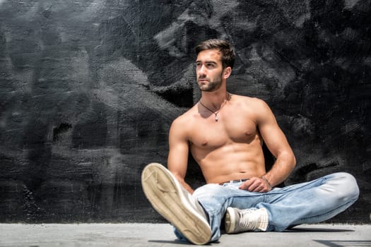 Handsome bearded shirtless young man sitting outdoors in urban environment