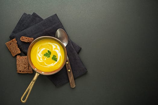 Healthy vegetable yellow cream soup on black background