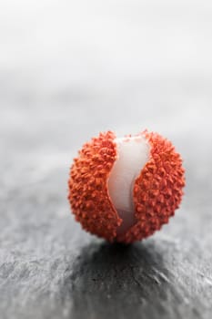 Studio shot of a lychee fruit with an open peel on slate plate.