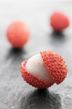 Three lychee fruits on slate plate. Front fruit with open peel on slate plate in focus. Rear fruits blurred as a bright silhouette.