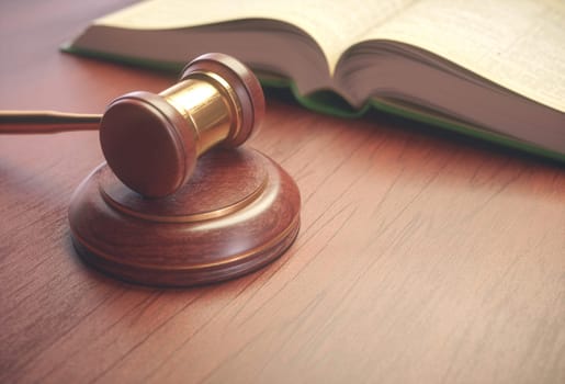 Wooden judge hammer with golden details and a legislation book beside.